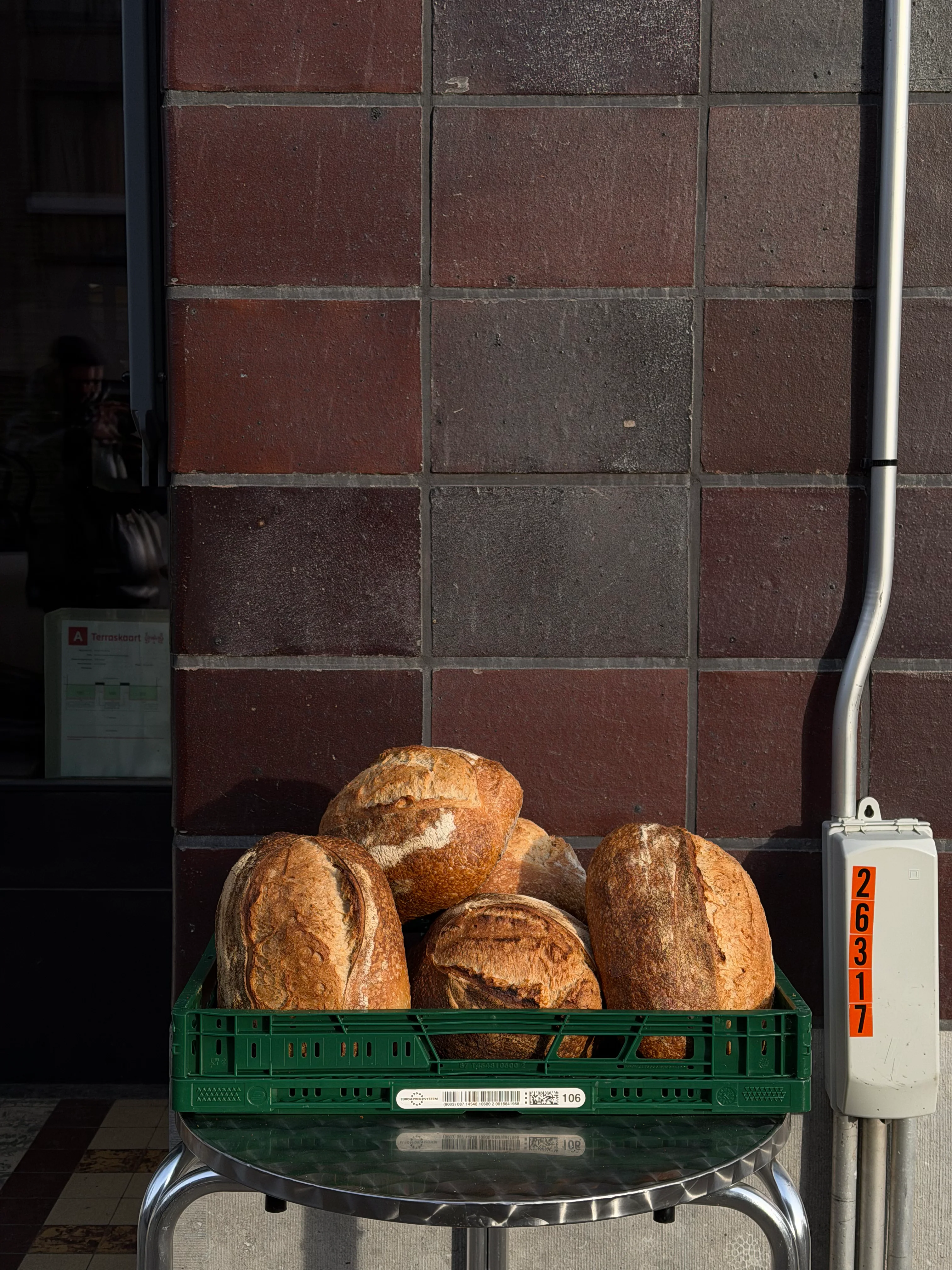 Large sourdough boules stacked in a green crate outside the bakery