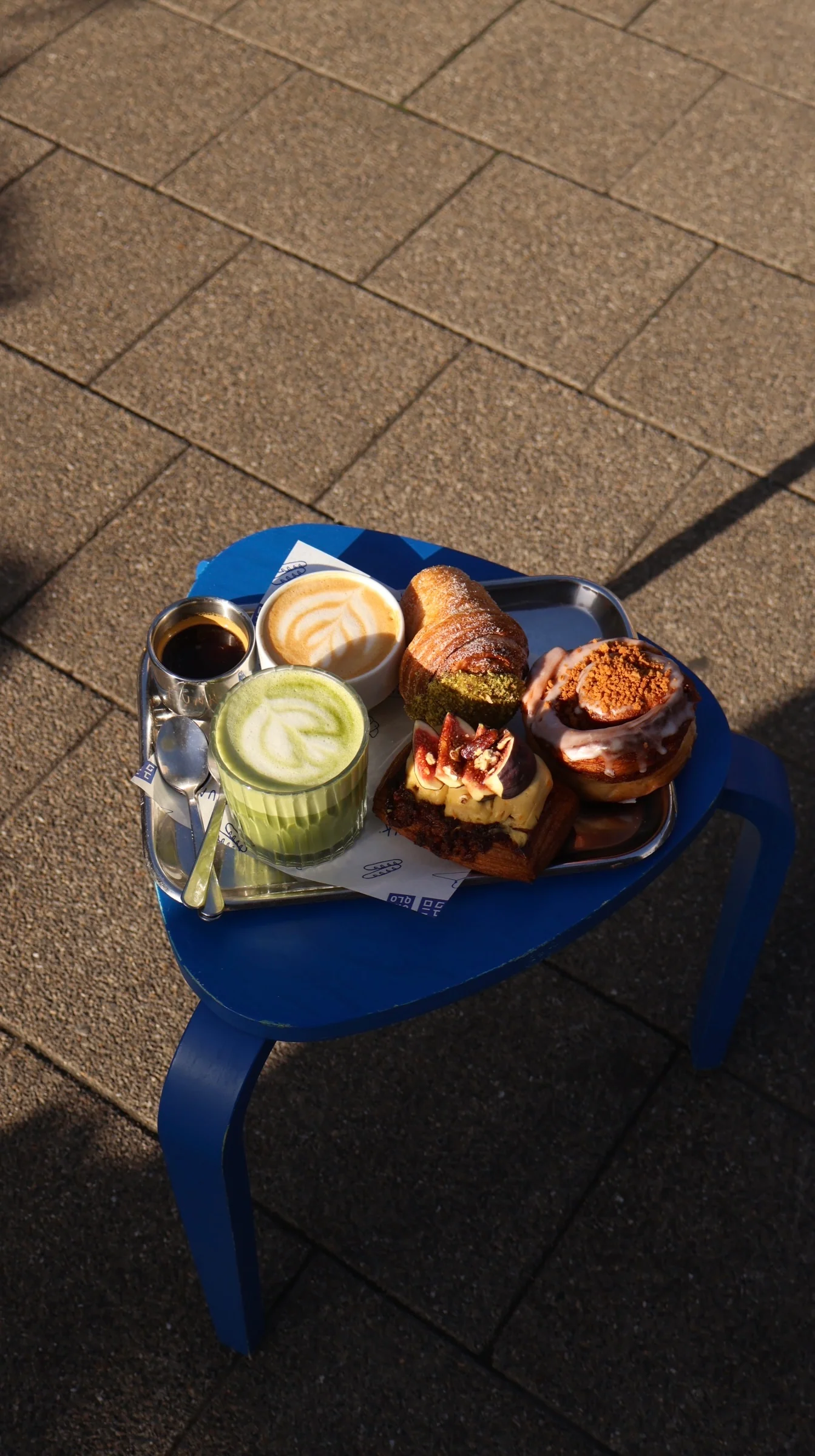 A tray of plant-based pastries — matcha latte, croissants and cinnamon buns — on a blue cafe table