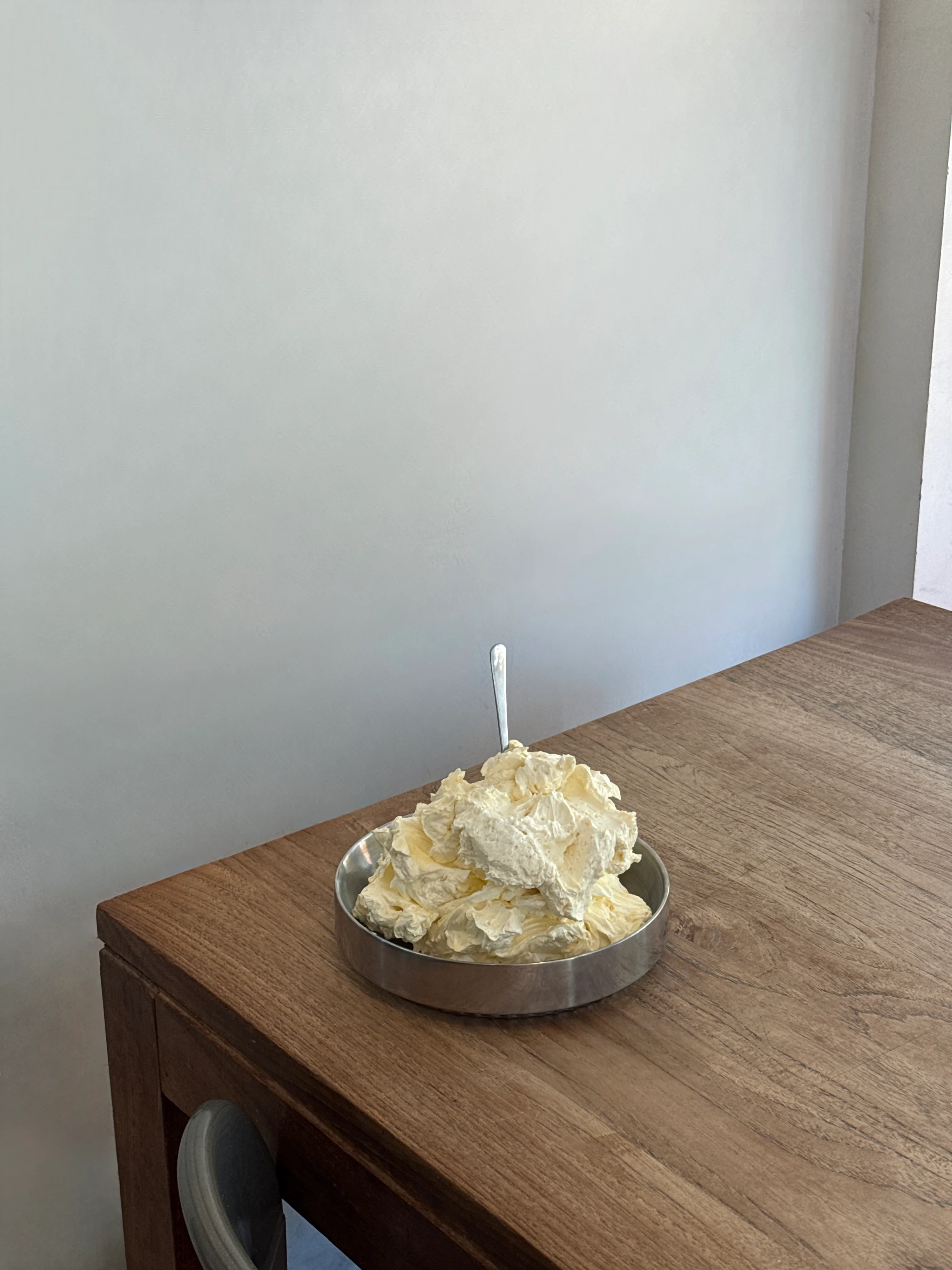 A bowl of fresh whipped butter with a spoon on a warm wooden table